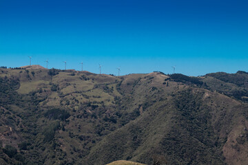 horizontal shot of beautiful landscape of a hill full of trees and wind towers generating electricity in the green hills of Escazu