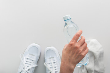 Female hand with a bottle of water, white sneakers and a towel on the floor, doing sports and training in the gym, active healthy lifestyle, top view, copy space
