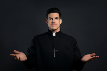 Priest wearing cassock with clerical collar on black background