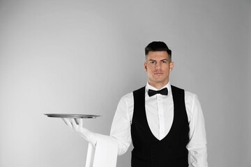 Handsome butler with tray on light grey background