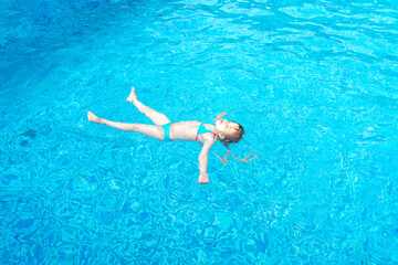 little girl swims in a swimming pool with blue water on a summer day