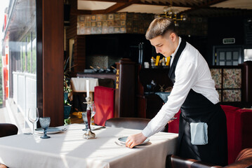 A young male waiter in a stylish uniform is engaged in serving the table in a beautiful gourmet restaurant. Restaurant activity, of the highest level.