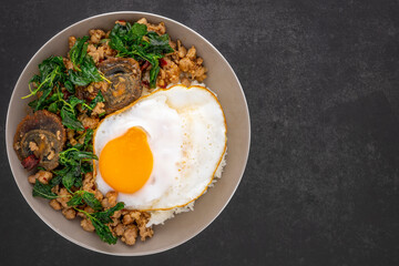 Khao Pad Ka Prao Kai Yeow Ma Kai Dao, Thai food, streamed rice with basil stir fried century egg, mince pork and fried egg in ceramic plate on dark grey texture background, top view