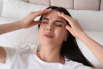 Fototapeta premium Young woman suffering from migraine in bed, above view