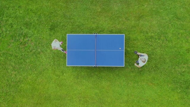 Aerial view people playing ping pong match outdoor. Top view man and woman playing table tennis on a green grass lawn. Aerial view outdoor sport