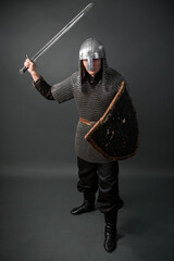 Medieval warrior of the late Viking era and the beginning of the Crusades. Knight in chain mail and helmet armed with a shield and sword isolated on a dark background.