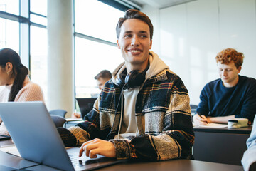 Student sitting in classroom with laptop - obrazy, fototapety, plakaty