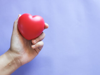 Selective focus hand holding red heart shape against purple background. Love concept.