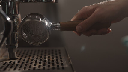 dark early morning man removes naked portafiler from coffee machine after making espresso