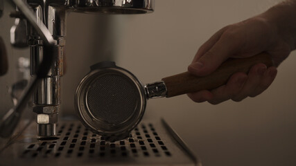 dark early morning man removes naked portafiler from coffee machine after making espresso