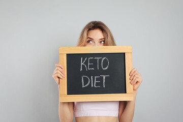 Woman holding blackboard with phrase Keto Diet on grey background