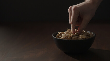 man take roasted pistachios from black bowl on walnut table