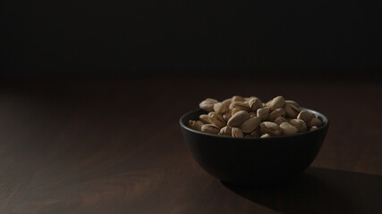 Slow motion handheld shot of roasted pistachios in black bowl on walnut table