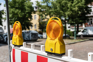 Zwei Gelbe Baustellenlampen befestigt an einer Absperrung in einem Wohngebiet im Querformat