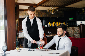 The waiter makes an exquisite serving of seafood salad, tuna and black caviar in a beautiful serving on the table in the restaurant. Exquisite delicacies of haute cuisine close-up.
