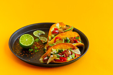 Mexican chicken and vegetables taco in black plate, flat lay on a yellow background, Latin American fast food