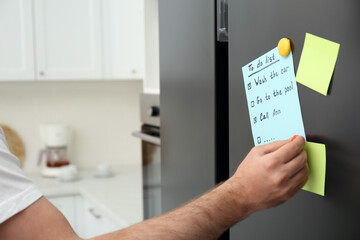 Man putting to do list on refrigerator door in kitchen, closeup