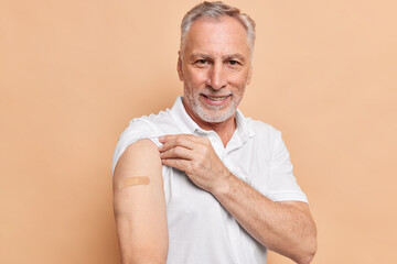 Old bearded man got vaccinated against coronavirus shows arms with adhesive plaster cares about...