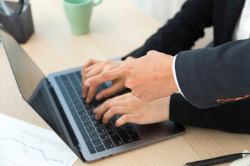 Asian businessman pointing finger at computer while woman worker working and typing.