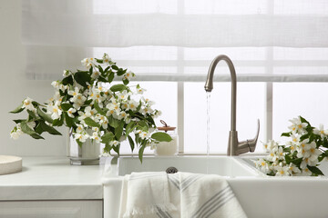 Bouquet of beautiful jasmine flowers in vase on countertop near kitchen sink