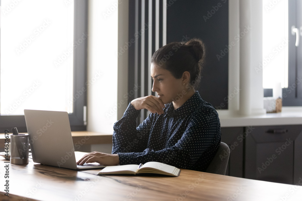 Canvas Prints focused indian student studying online from home, watching webinar on laptop, doing and thinking ove