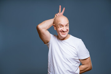 an adult bald man in a white T-shirt poses emotionally on a blue background. Portrait taken...