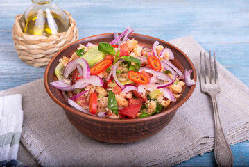 Homemade authentic Tuscan panzanella salad in a bowl on a table with a fork and a jug of olive oil, close-up