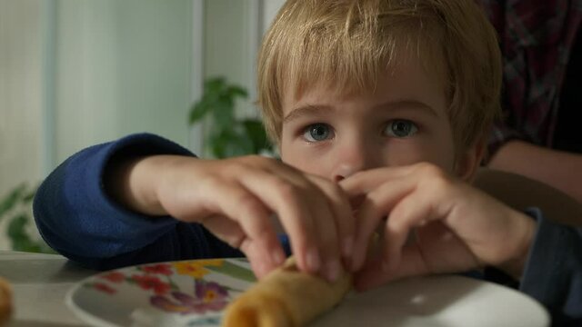 Cute Little Child Eats Pancakes Rolled up with Filling Food Meal on Dish Plate. Boy Sitting Near at Table in Kitchen. 2x Slow motion 60fps 4K