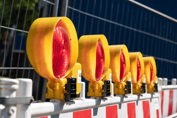 Fünf rote  Baustellenlampen in Reihe befestigt an einer Absperrung vor einem Baustellenzaun im...