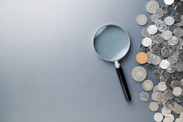 Magnifying glass and a pile of money coins on gray background with copy space