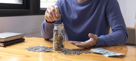 Man puts a coin dollar in a jar, Saving money for future growth and knowing how to manage your spending wisely, Saving money for business growth or long-term profitability.