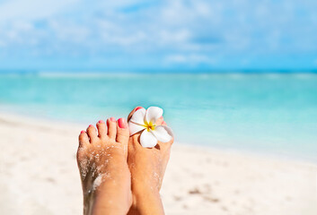 Relaxing bare female feet with white  frangipani flower by the water on sea shore, with copy space