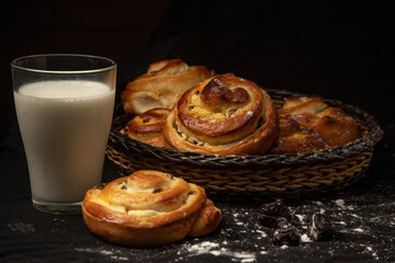 buns in a wicker bowl and a glass of milk on a dark background