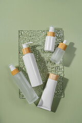 Pump bottle, cream tube, and dropper on green background. Cosmetic container mock-ups. Background for branding and packaging presentation. Natural skincare beauty product concept.