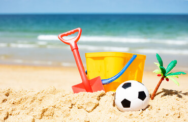 Bucket with toys, football ball, palm tree in sand