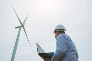 Engineers windmills wearing face mask and  working on laptop with the wind turbine in background