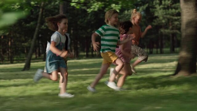 Side view of happy carefree kids running on green grass in park. Little friends having fun attempting to run faster than friends. Group of active children playing together