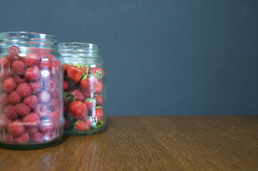 Red ripe raspberries and strawberries in glass jars on a wooden table.