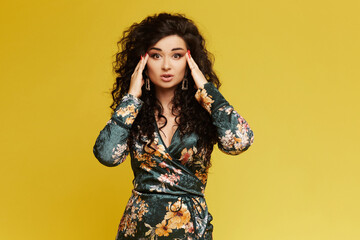 Beauty fashion model girl in a trendy dress, with bright makeup, amazed young brunette woman isolated on yellow background, posing