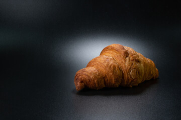 Fresh croissant on a black slate background. Concept for the production and baking of bakery products. Copy space