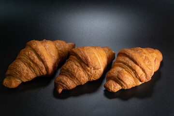 Lot of fresh croissant on a black slate background. Concept for the production and baking of bakery products. Copy space