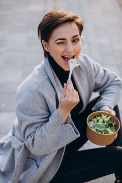 Young Woman Eating Salad Outside The Street