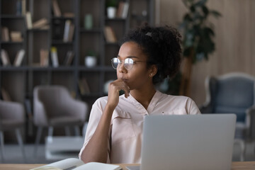 Thoughtful African American woman in glasses looking to aside touching chin, pondering project...