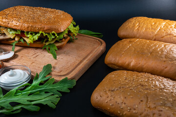 Fresh and tasty Italian panini, sandwich with chicken and vegetables, sauce, salad, mushrooms, tomato and cucumber, on wooden spacing, plate. Black background