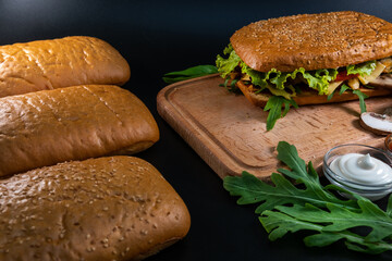 Fresh and tasty Italian panini, sandwich with chicken and vegetables, sauce, salad, mushrooms, tomato and cucumber, on wooden spacing, plate. Black background