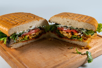 ciabatta sandwich with chicken and vegetables on wooden spacing, plate isolated on white background. Concept for the production of fast food bread. cut in half. Bakery products