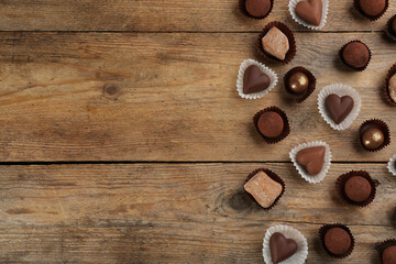 Different delicious chocolate candies on wooden table, flat lay. Space for text