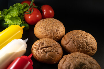 Bun, hamburger bread and burger ingredients. Sauce, Cheese, Salad and Vegetables. Concept for the production of fast food bread. Bakery products. on black background.
