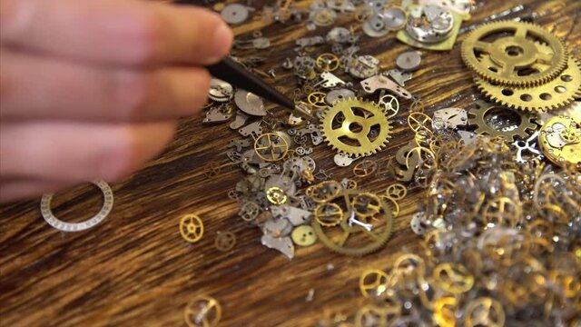 Master moves mechanicals details with tweezers. Woman watchmaker works with gears, close up, soft selective focus. Precision and meticulousness concept.