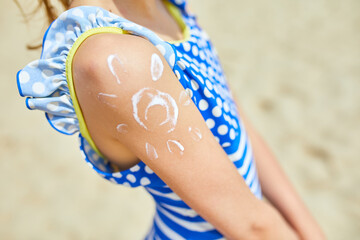Little girl with applying sunscreen on shoulder in form of the sun standing on the beach